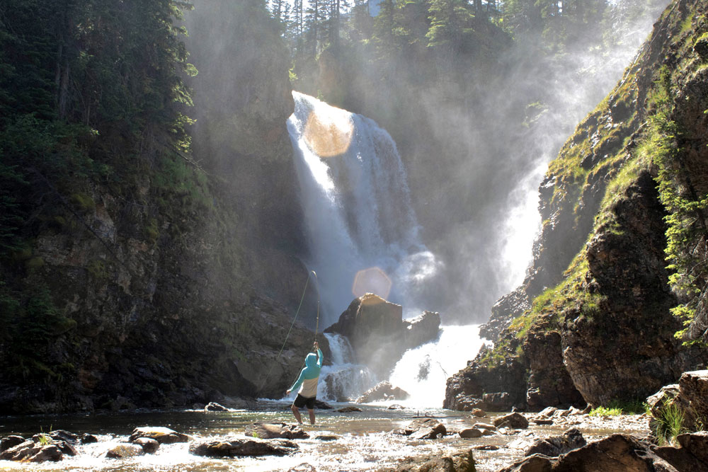 Fly fisherman under a waterfall