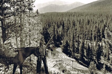 Cecil Garland stands with horse overlooking forest and river